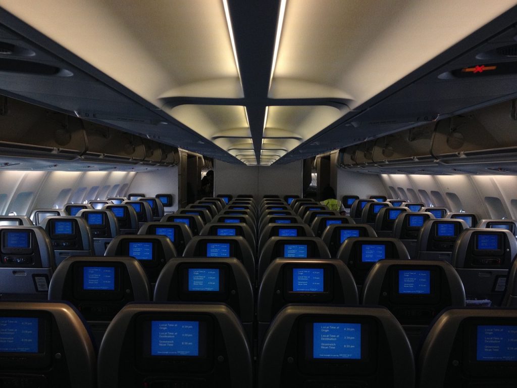 An empty wide-body aircraft cabin with crew in the back preparing for a flight.